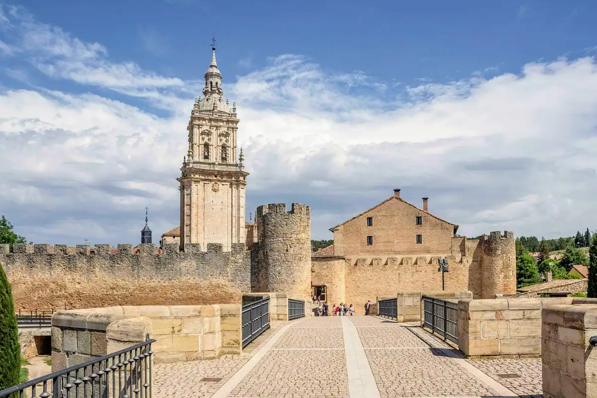Turn de catedrală și zid de fortificație deasupra acoperișurilor unui oraș vechi, văzut de pe alee
