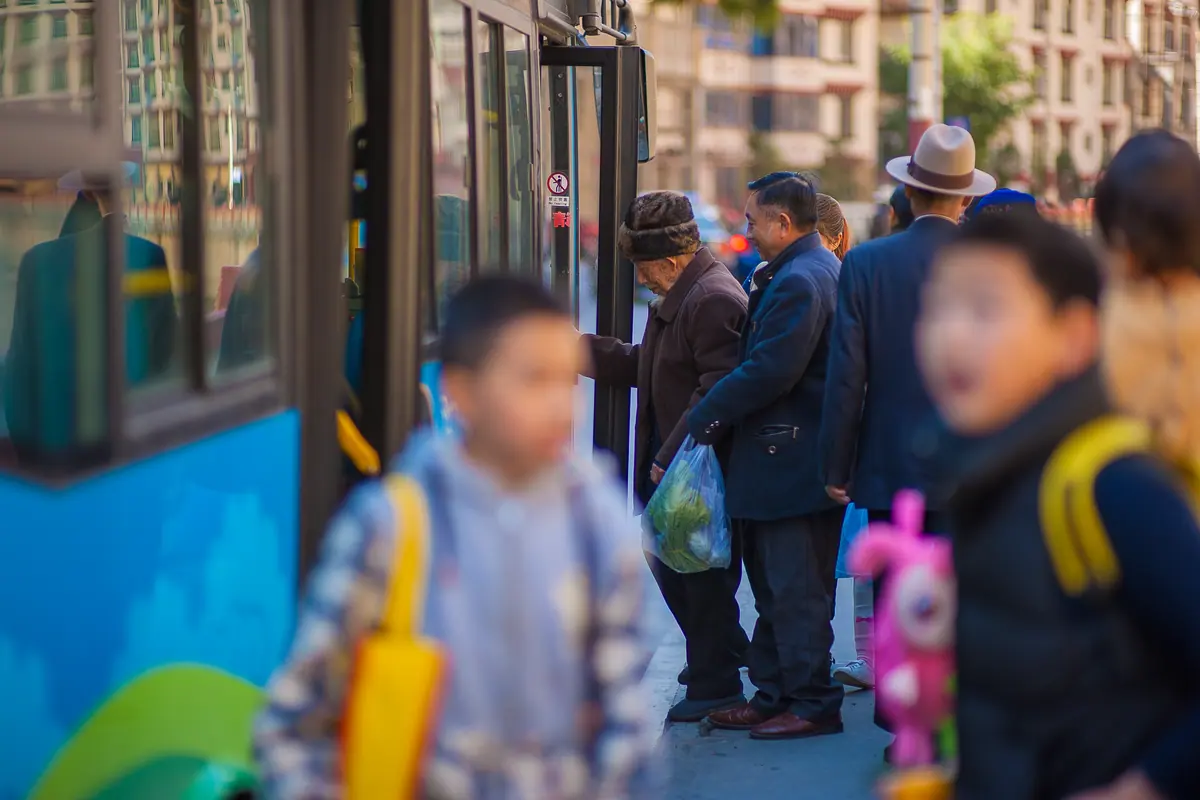 Călători, printre care copii cu ghiozdane, urcă într-un autobuz albastru la stație