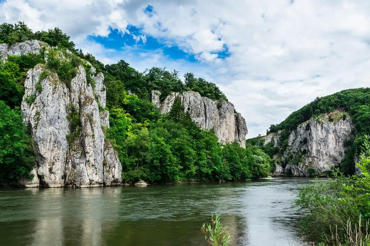 Stânci calcaroase și pădure pe malul Dunării, în zona Clisurii, sub un cer cu nori