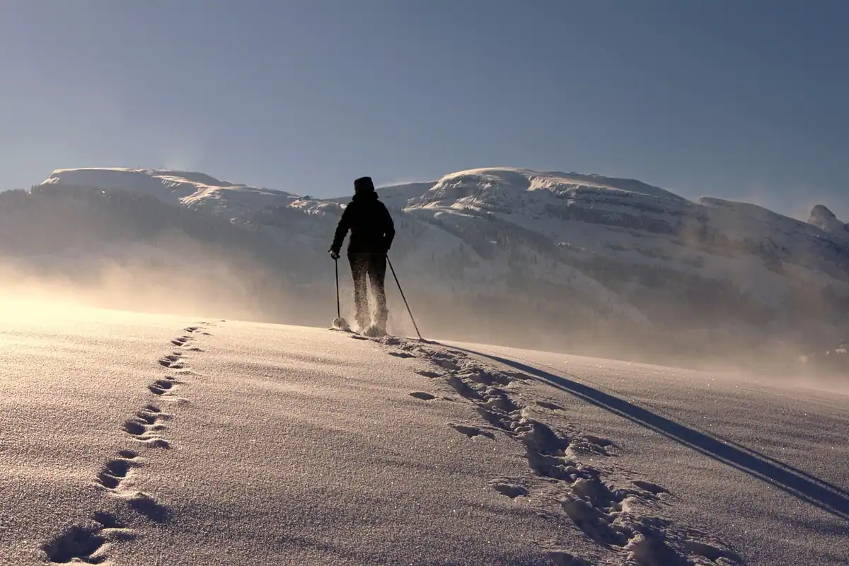 Bețe de trekking sprijinite pe stâncă, cu munți înzăpeziți și urme de pași în fundal