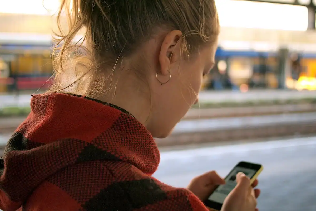 Femeie care se uită la telefon pe peron, în timp ce își caută biletul de tren