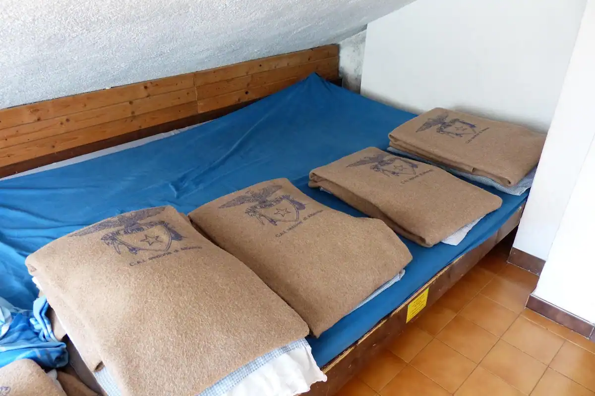 Pat de cabană cu așternut albastru și perne de culoare bej, într-o cameră simplă