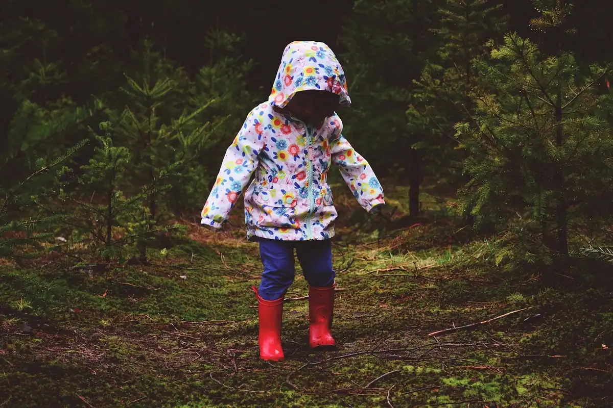 Copil în hanorac colorat și cizme roșii care merge pe o potecă prin pădure
