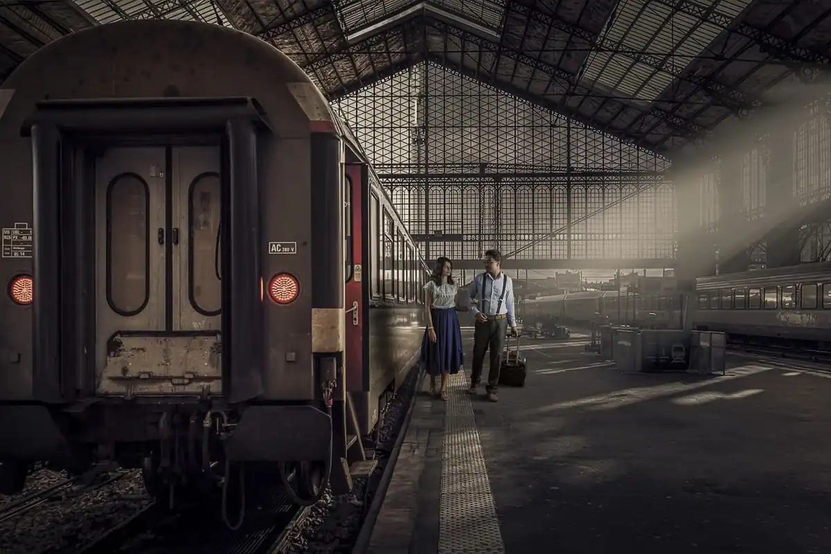 Vagon de tren vechi pe peron, cu doi călători care se îndreaptă spre el
