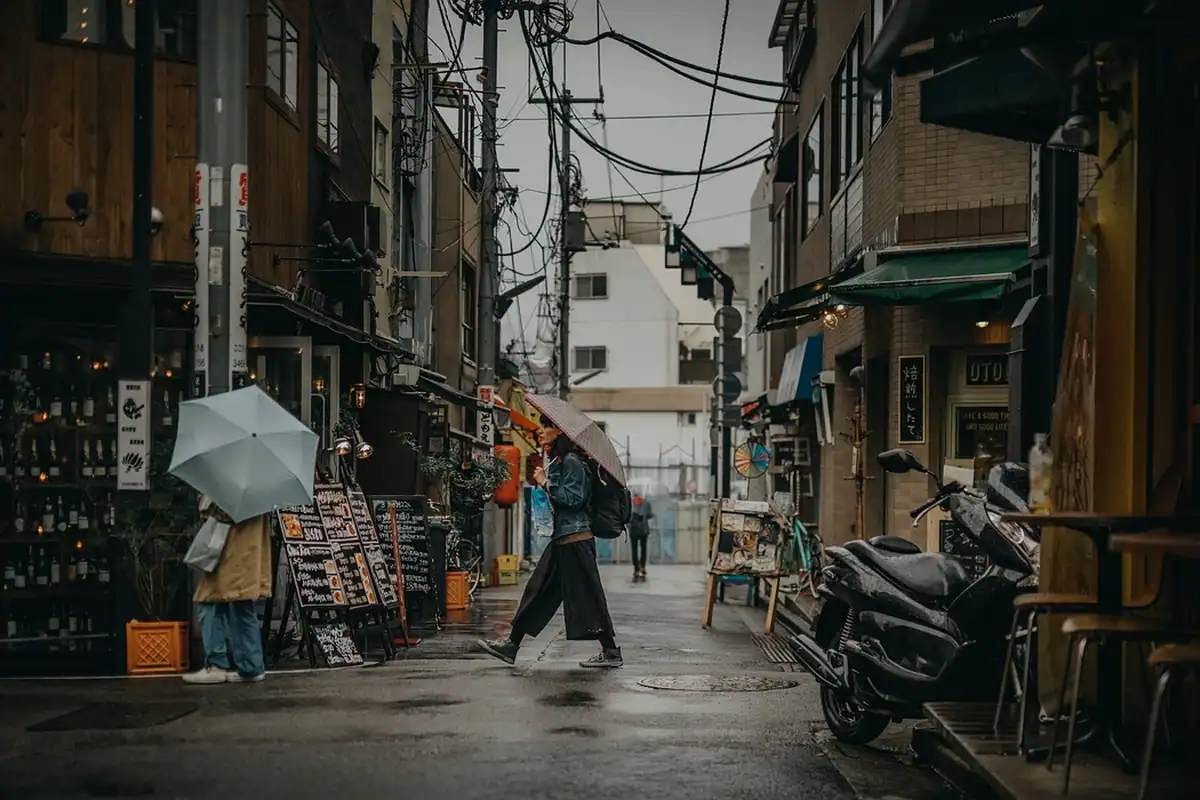Femeie cu umbrelă pe o stradă udă de oraș, printre tarabe de piață, într-o zi ploioasă
