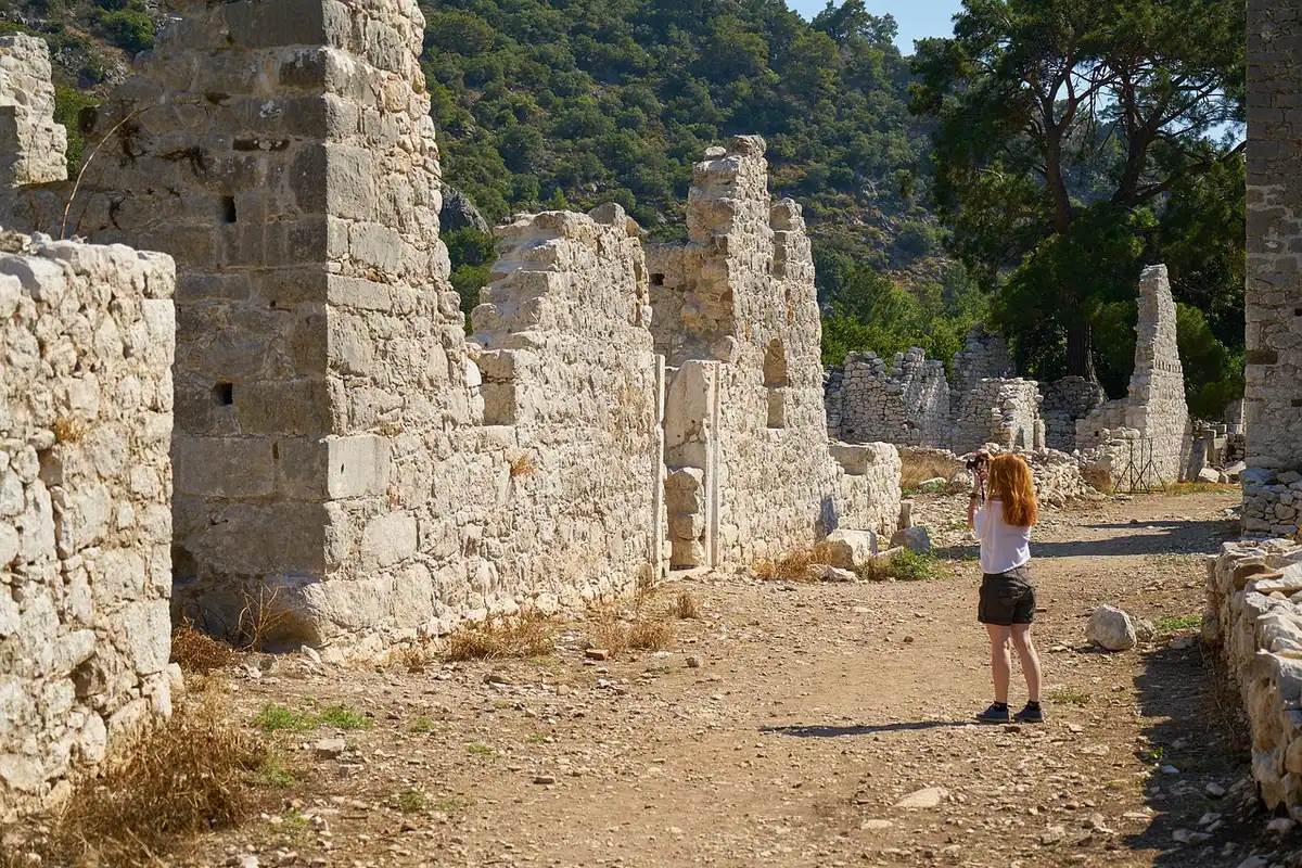 Turistă fotografiind ruine antice de piatră într-un peisaj muntos împădurit, într-o zi de vară