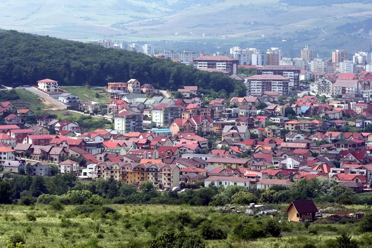 Oraș întins la poalele unor dealuri, cu case cu acoperișuri roșii și blocuri în fundal