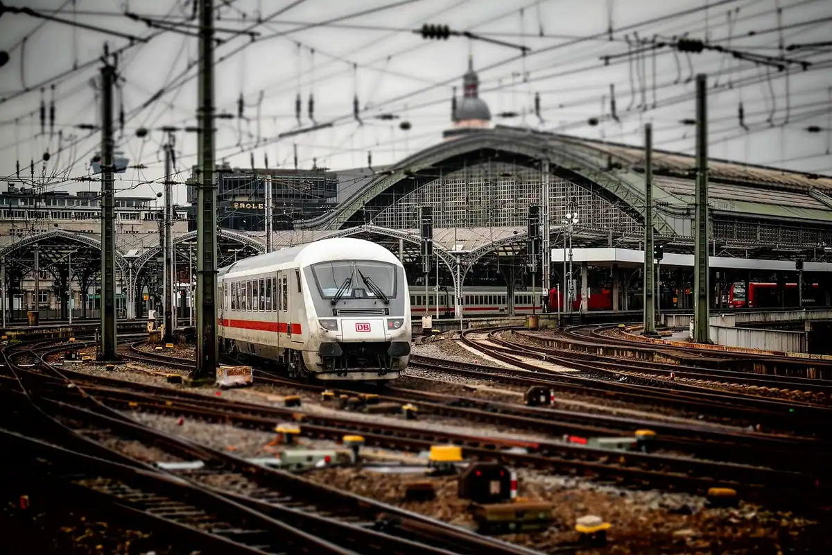 Gară mare cu linii ferate, tren oprit și structură metalică, punct de plecare spre munte