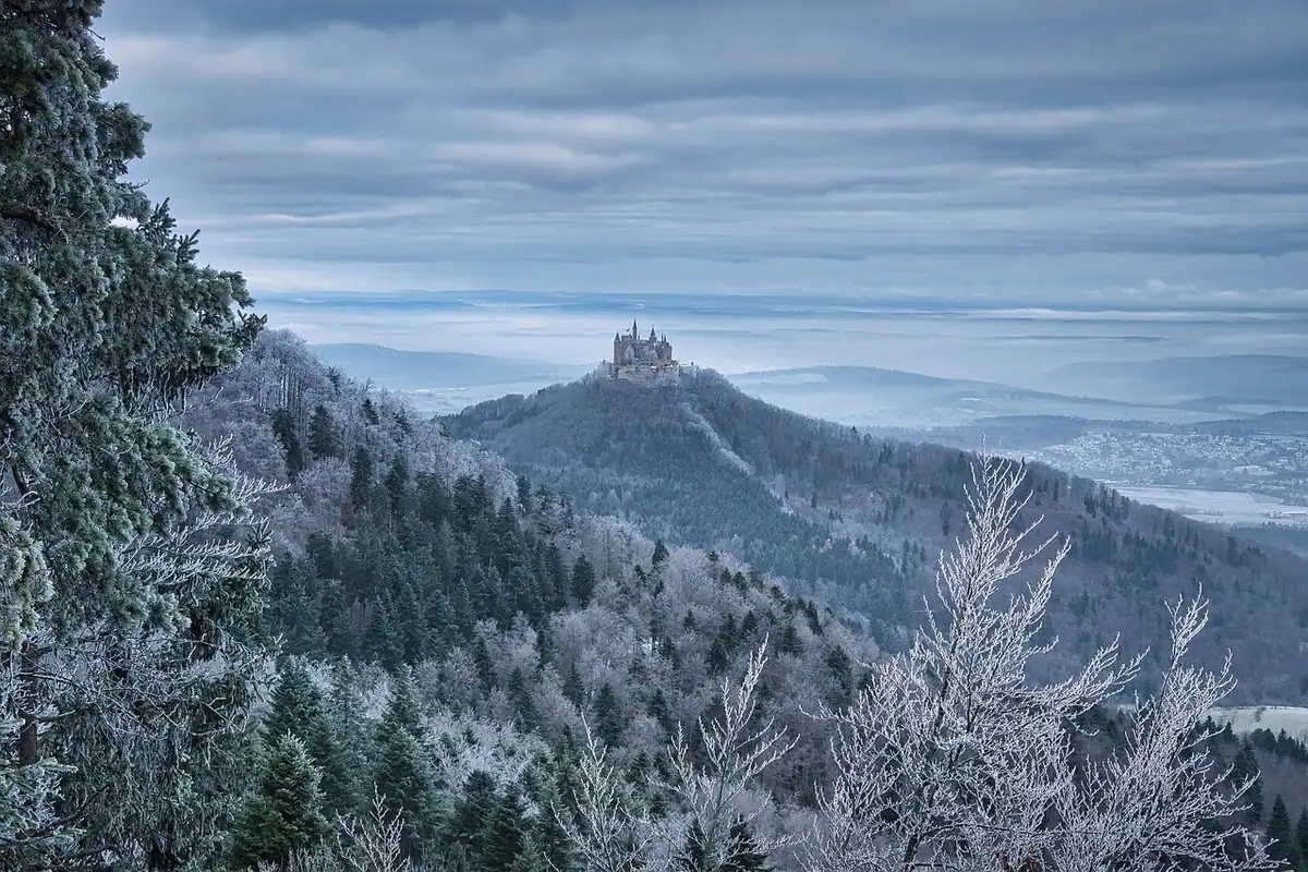 Castel medieval pe un deal stâncos, învăluit în ceață și brumă, cu turnuri vizibile