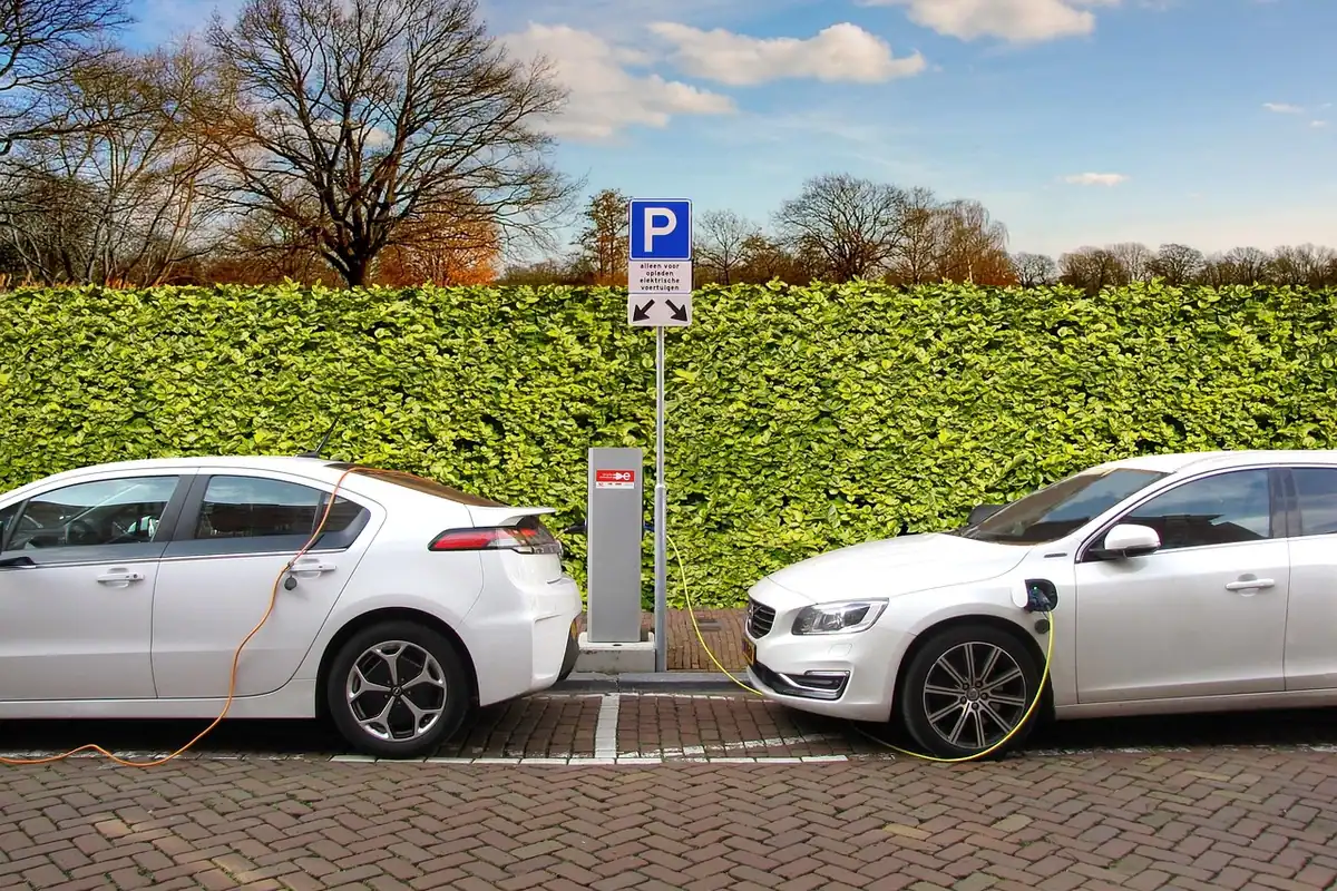 Mașină electrică parcată la o stație de încărcare, cu cablul conectat, pe o stradă urbană