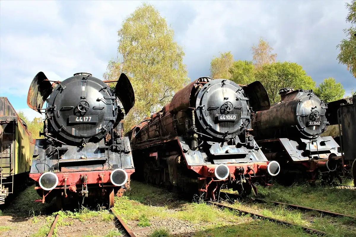 Trei locomotive vechi cu aburi, oprite pe linii ruginite într-un muzeu feroviar