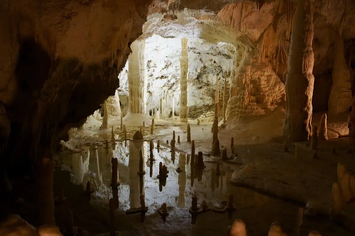 Peșteră cu stalactite și stalagmite, cu o baltă în care se oglindesc pereții