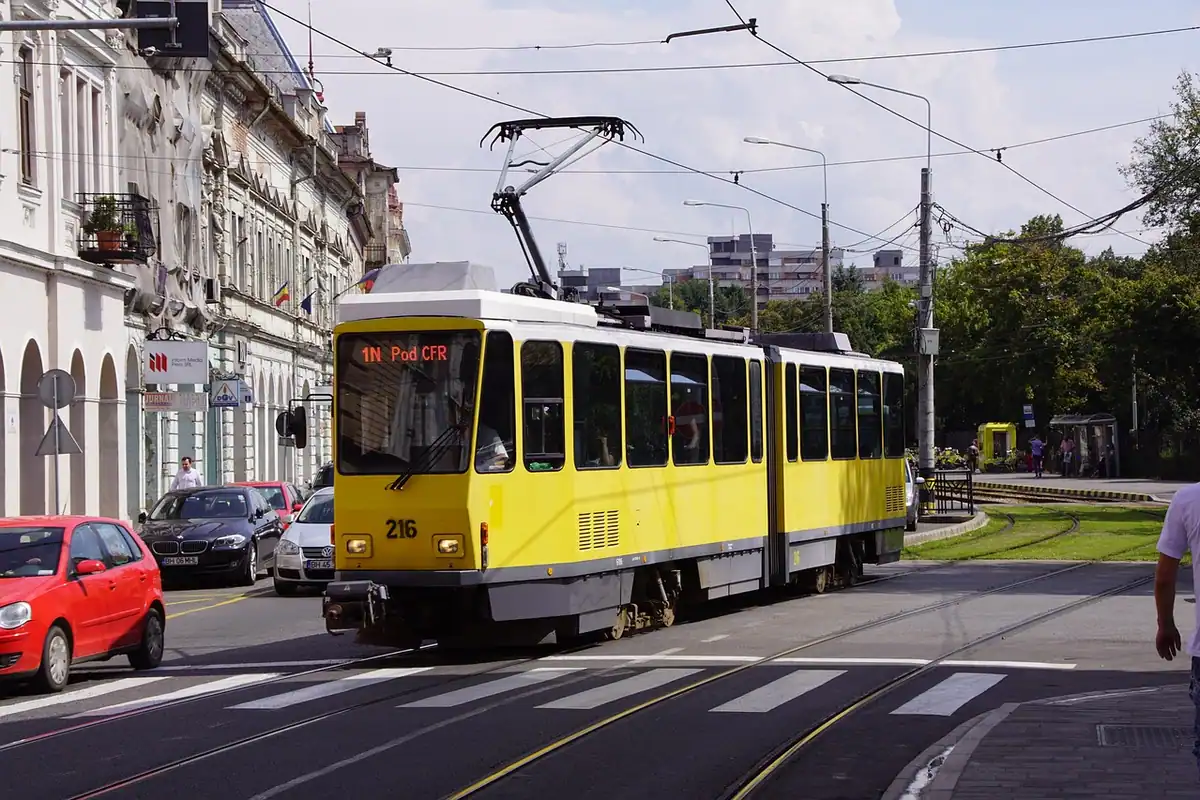Tramvai galben circulând pe o stradă din oraș, cu mașini și clădiri în jur