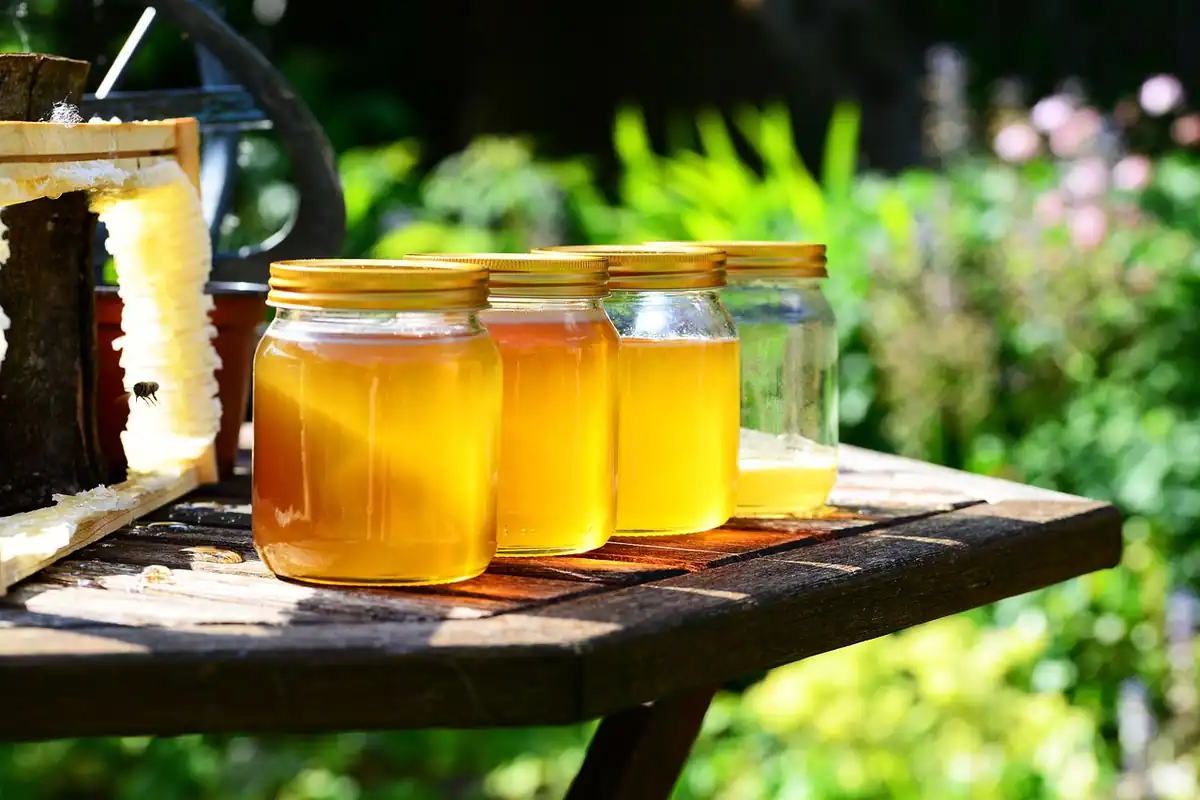 Borcane de sticlă cu miere aurie, așezate pe o masă de lemn, la o tarabă cu produse locale