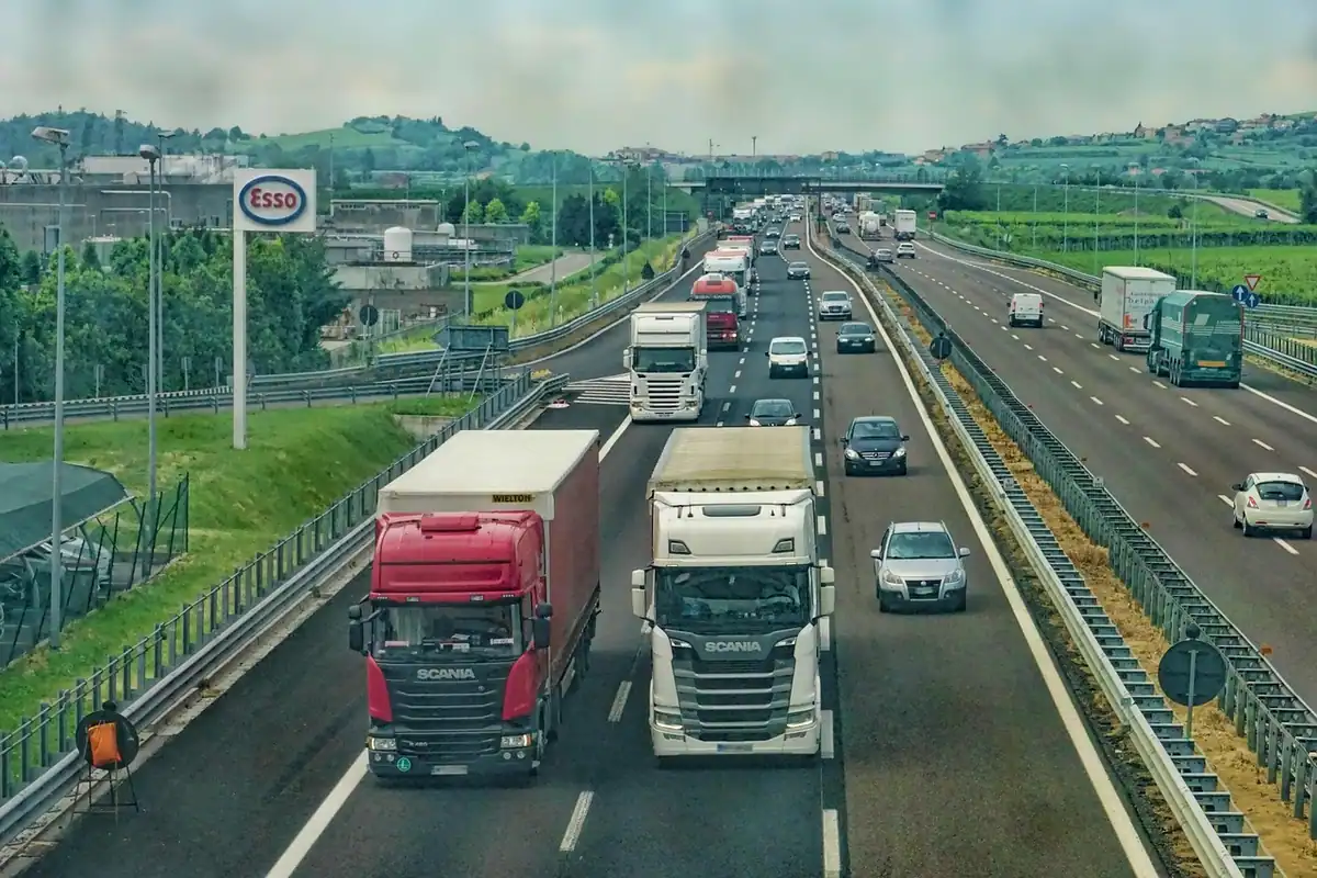 Autostradă cu camioane și mașini în trafic, pe sub un pasaj cu indicatoare de taxă