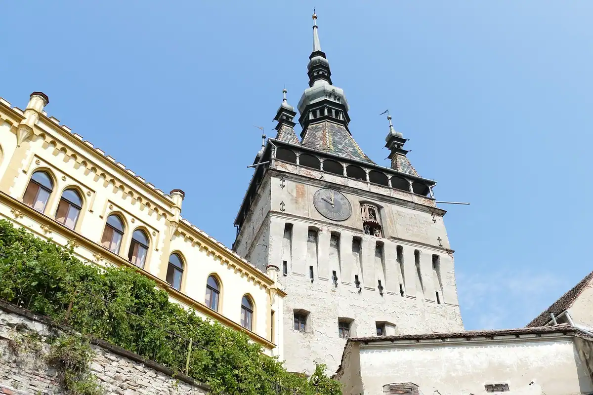 Turnul cu ceas din Sighișoara, cu clădiri galbene și cer senin deasupra