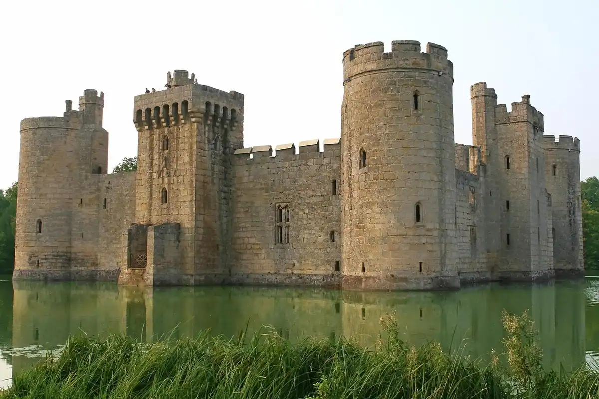 Fortăreață medievală cu zid de piatră înconjurat de un șanț cu apă și iarbă verde