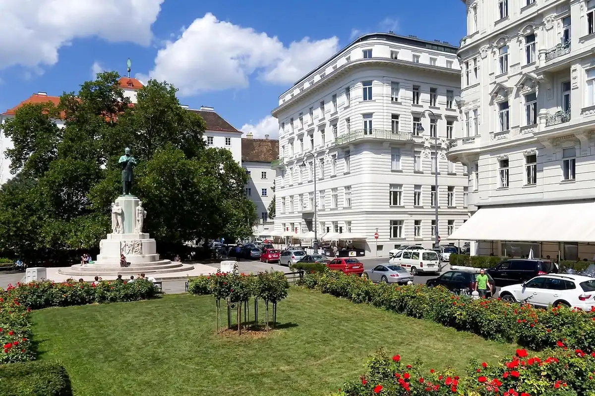 Scuar cu trandafiri și flori în fața unor clădiri istorice, cu iarbă verde și copaci