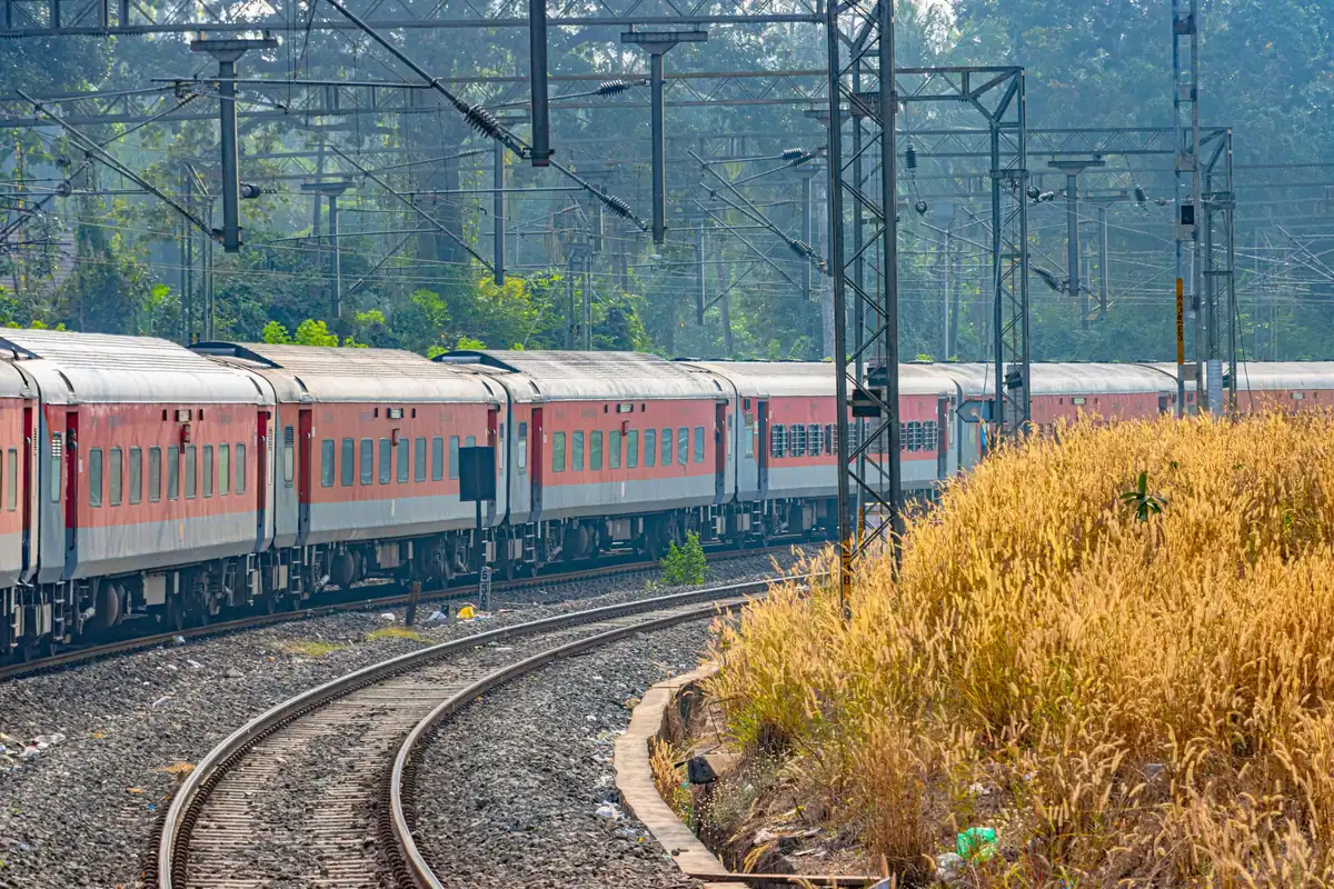 Tren de călători cu vagoane roșii pe o cale ferată electrificată, printre copaci