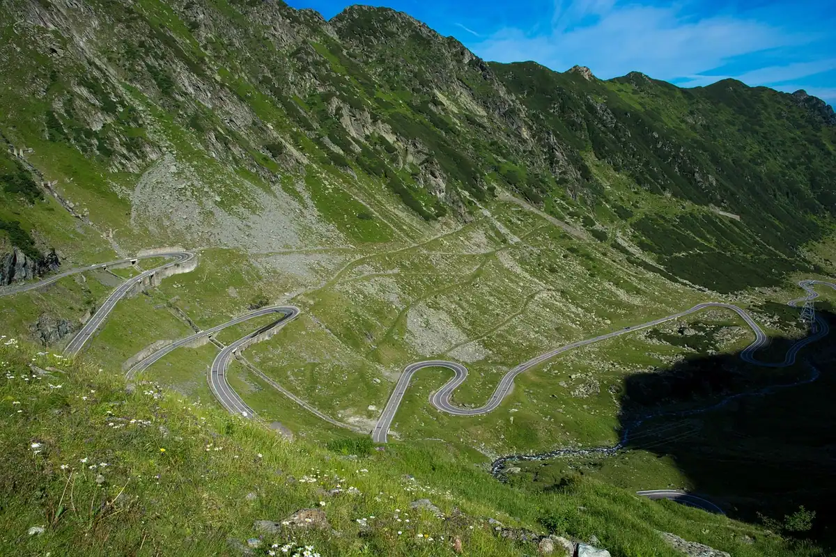Drum în serpentine pe versantul verde al unui munte, într-o zi însorită
