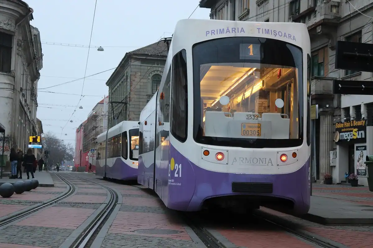 Tramvai modern alb și mov circulând pe șine, printr-o stradă din oraș