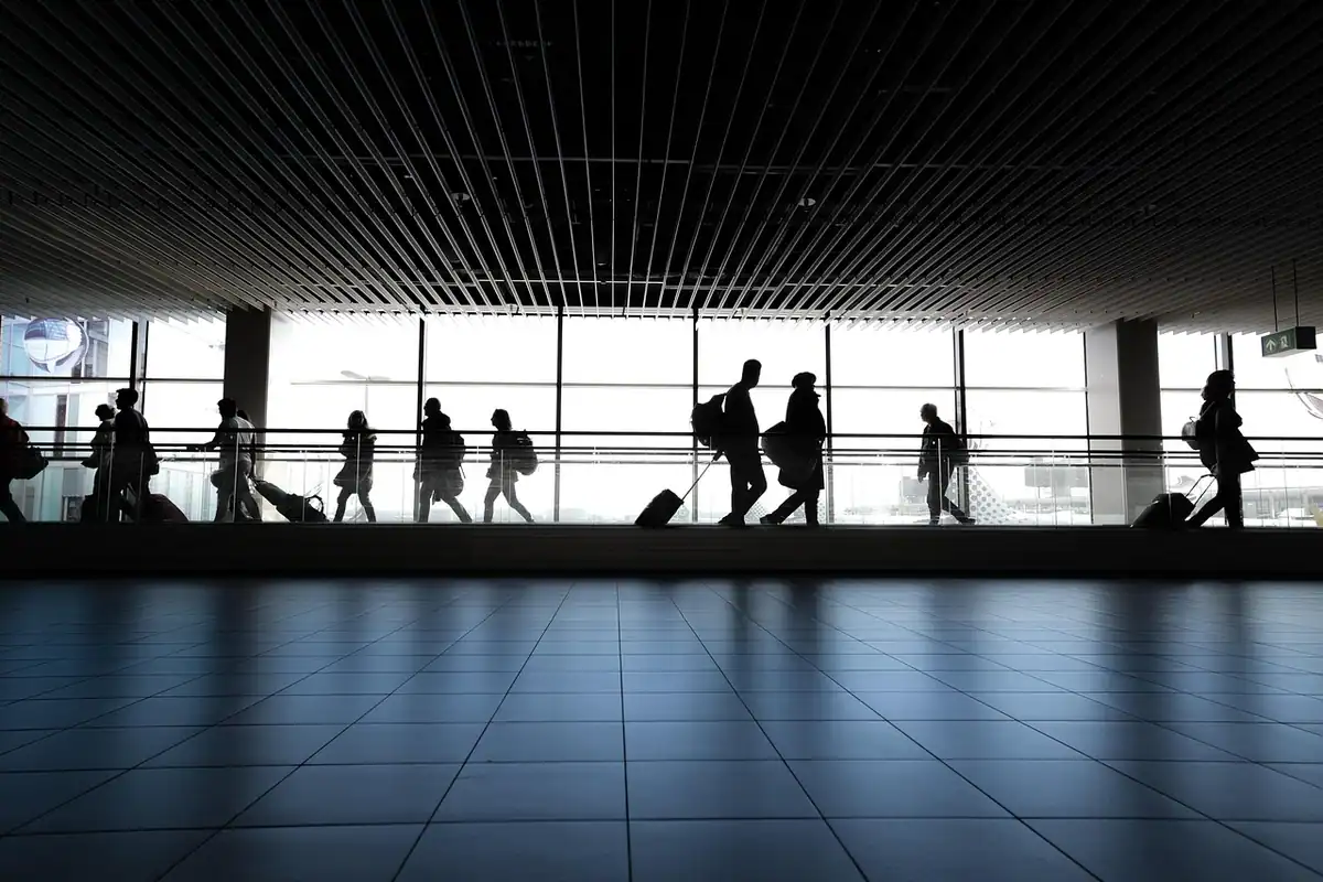 Siluete de călători cu bagaje, așteptând într-un terminal mic de aeroport
