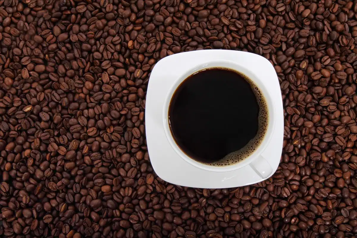 Ceașcă de cafea neagră și boabe de cafea pe masă, lângă o hartă a centrului vechi